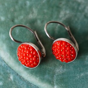 May include: A pair of silver earrings with red bead clusters. The earrings have a simple hook design.