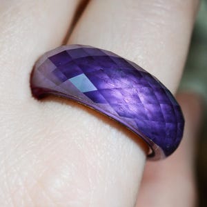 Op de afbeelding: Een dieppaarse ring met een gefacetteerd oppervlak en een geometrisch ruitpatroon. De band heeft een afgerond, koepelvormig profiel en een doorschijnend uiterlijk, waarbij het licht reflecteert op de vele schuine vlakken voor textuur.