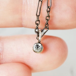 May include: Close-up of a small, antique silver necklace with a single, round, clear gemstone pendant. The chain is made of small, dark silver links. The pendant is a faceted, clear stone.