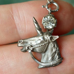Peut inclure: Pendentif licorne argenté avec une pierre précieuse claire et facettée au-dessus de sa tête. La licorne a une crinière, une corne et un bridon détaillés. Le pendentif est attaché à une petite chaîne argentée.
