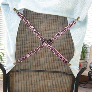 May include: A black metal patio chair with a brown mesh back and seat. A light blue towel with a white pattern is secured to the back of the chair with two pink and black patterned straps.