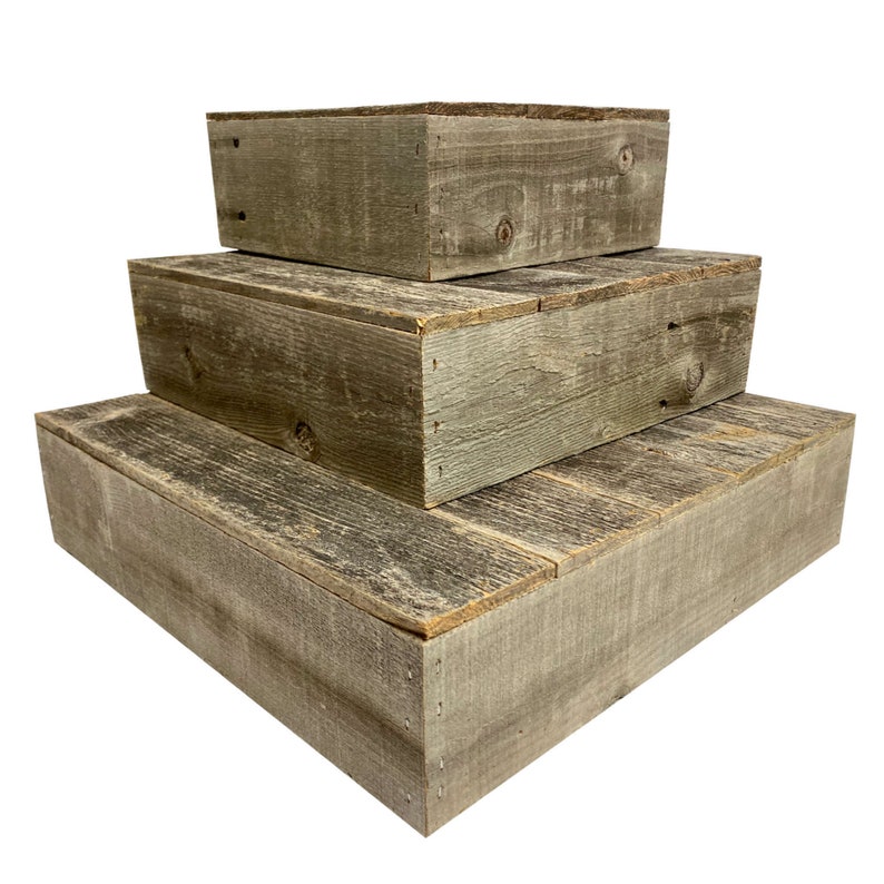 May include: A set of three rustic wooden boxes stacked on top of each other, creating a tiered display. The boxes are made of weathered wood with a natural grey finish.