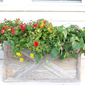 May include: A rustic wooden planter box with a weathered gray finish. The planter is filled with a variety of colorful flowers, including red, yellow, and pink.