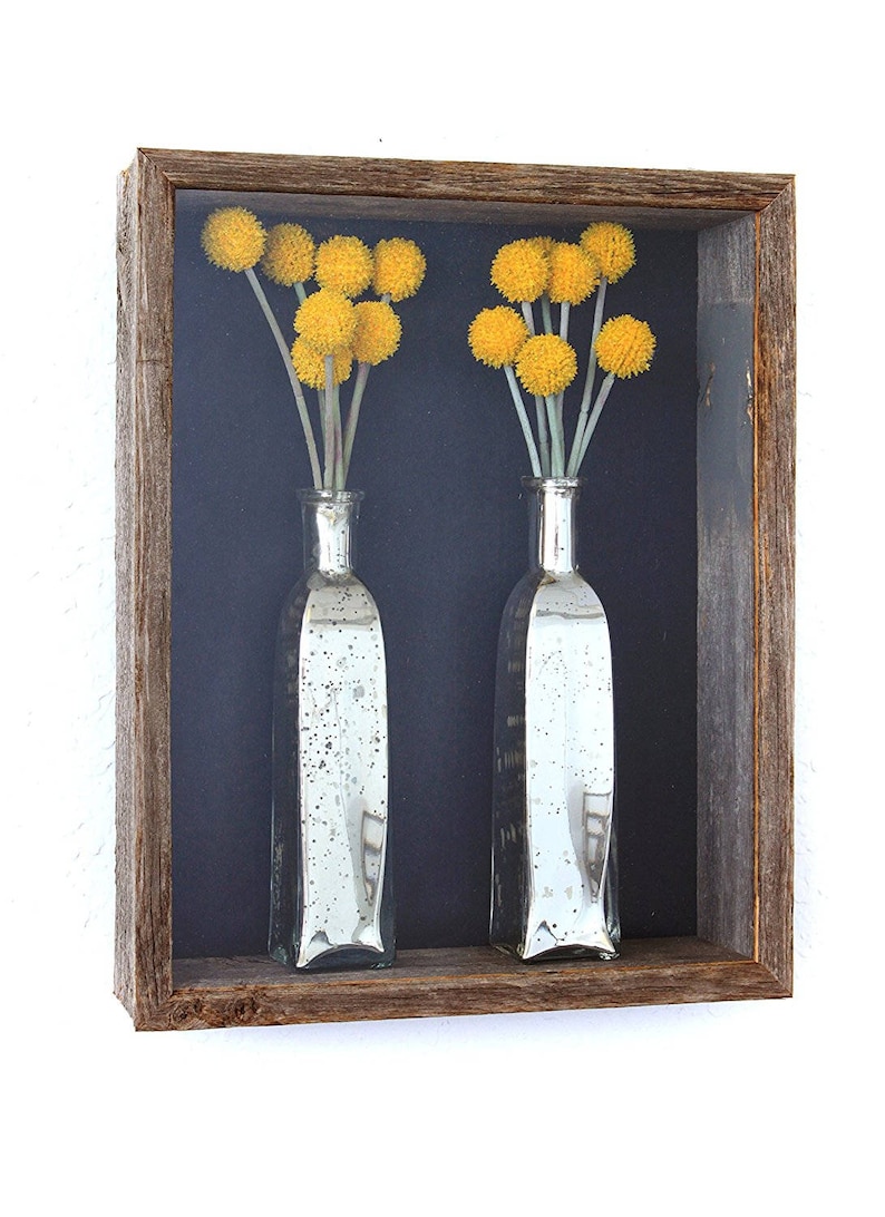 May include: Two silver glass vases with yellow dried flowers inside a rustic wooden frame. The background is a dark blue.