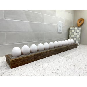 May include: A rustic wooden egg holder with 12 white eggs. The holder is made of reclaimed wood and has a natural, weathered finish.