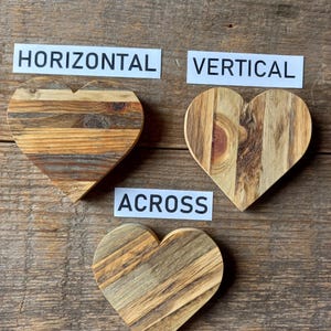 May include: Three wooden heart-shaped decorations with varying wood grain patterns. The hearts are arranged with the words "HORIZONTAL", "VERTICAL", and "ACROSS" on white labels. The background is a rustic wooden surface.