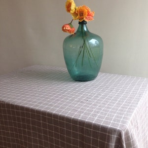 May include: A blue glass vase with a textured surface holds a bouquet of orange and yellow poppy flowers on a brown and white checkered tablecloth.
