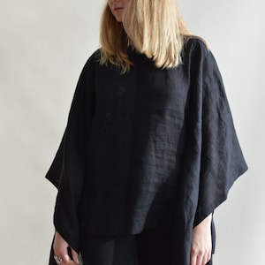 May include: A black linen poncho with a loose, flowing fit. The poncho is worn over black pants.