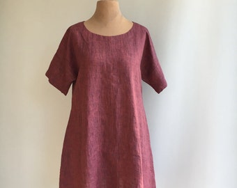 Puede incluir: Un vestido de lino burdeos con cuello redondo y mangas cortas. El vestido tiene un corte holgado y llega hasta la rodilla.
