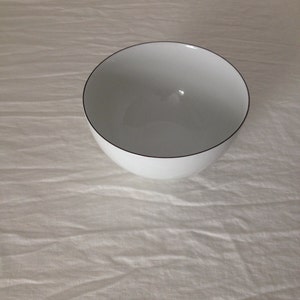 May include: A white ceramic bowl with a black rim. The bowl is empty and sitting on a white surface.