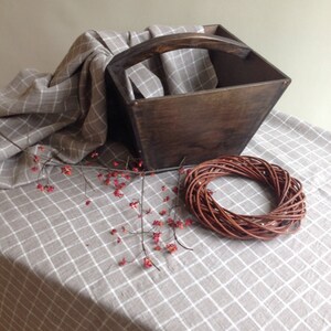 May include: A wooden box with a handle, a woven wreath, and a sprig of red berries on a beige and white checkered tablecloth.