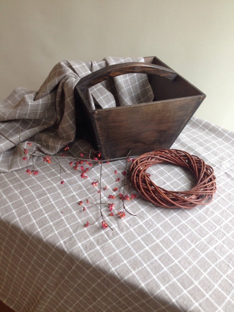 May include: A wooden box with a handle, a woven wreath, and a sprig of red berries on a beige and white checkered tablecloth.