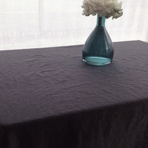 May include: A dark gray linen tablecloth with a teal glass vase filled with white flowers.
