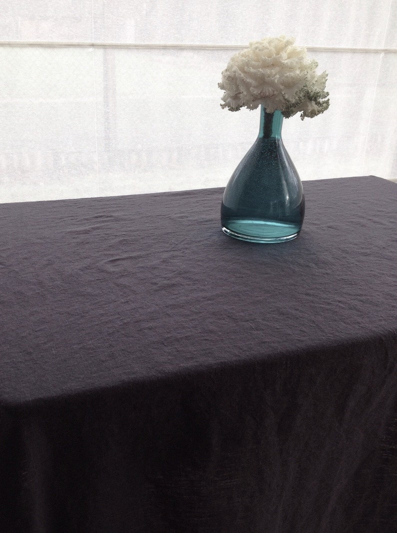 May include: A dark gray linen tablecloth with a teal glass vase filled with white flowers.
