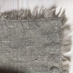 May include: A close-up of a piece of natural burlap fabric with a frayed edge. The fabric is a light brown color and has a rough texture.