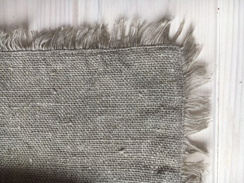 May include: A close-up of a piece of natural burlap fabric with a frayed edge. The fabric is a light brown color and has a rough texture.