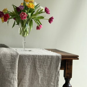 May include: A bouquet of colorful tulips in a clear glass vase on a rustic wooden table with a linen tablecloth.