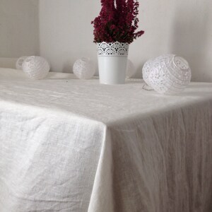 May include: A white tablecloth with a white vase filled with pink heather flowers. There are three white paper lanterns on the table.