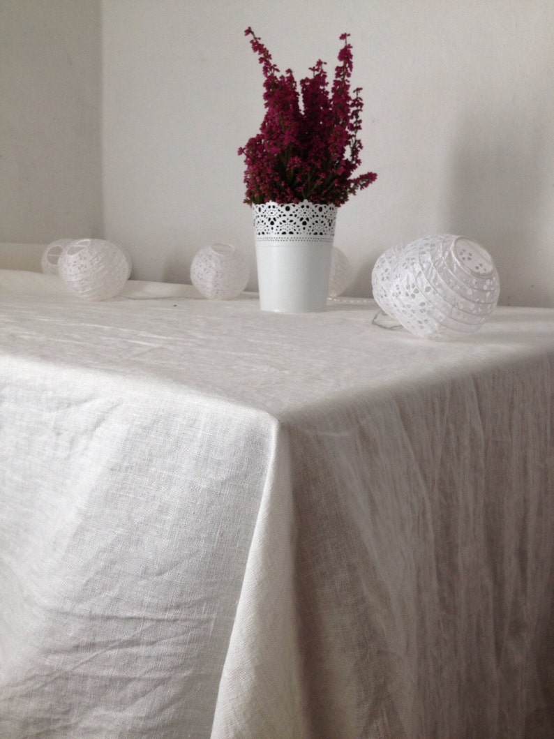 May include: A white tablecloth with a white vase filled with pink heather flowers. There are three white paper lanterns on the table.