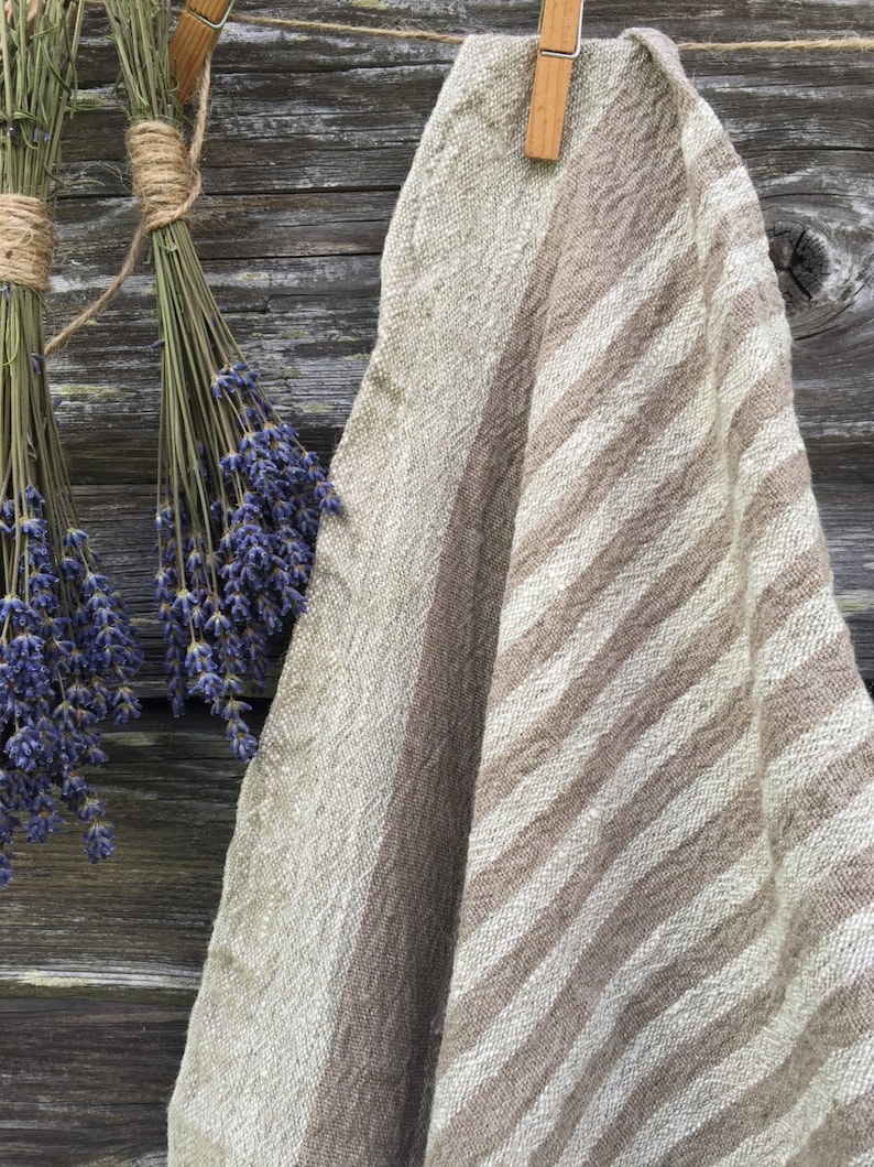 May include: A brown and white striped linen throw blanket hanging on a wooden fence with dried lavender bundles.