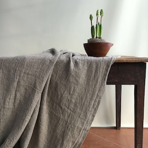 May include: A brown wooden table with a gray linen tablecloth draped over it. A small potted plant with green leaves is on the table.