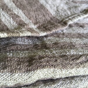 May include: Close-up of a brown and white striped fabric with a textured weave. The fabric is folded over itself, showing the layers of the weave.