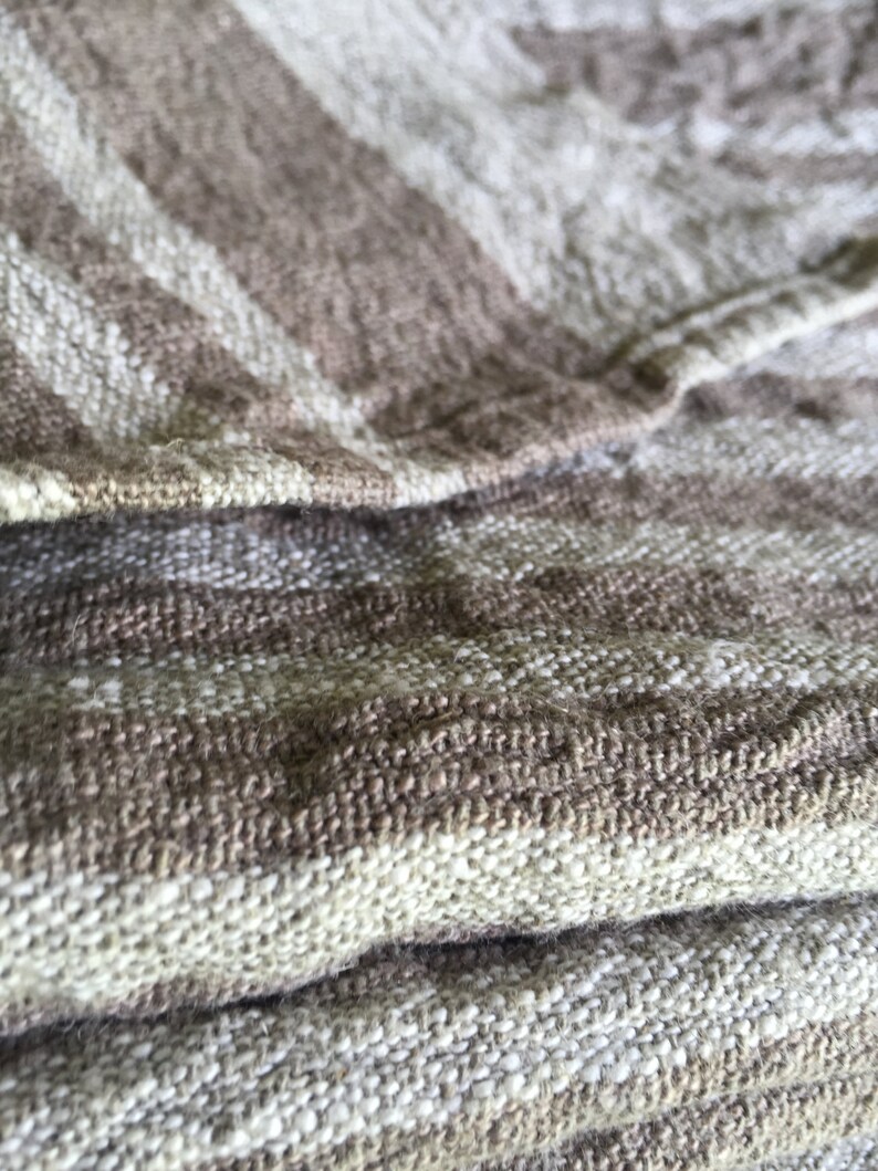 May include: Close-up of a brown and white striped fabric with a textured weave. The fabric is folded over itself, showing the layers of the weave.