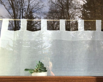 May include: White sheer curtains with a row of small tabs along the top edge. The curtains are hanging in a window and a small green plant is visible in the bottom center of the image.