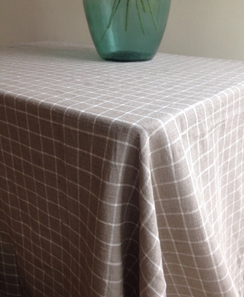 May include: A beige linen tablecloth with a white checkered pattern. The tablecloth is draped over a table and has a slight wrinkle in the center.