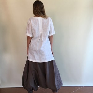 May include: A white linen top with a back pleat and short sleeves paired with brown linen pants. The pants have a wide leg and a gathered design.