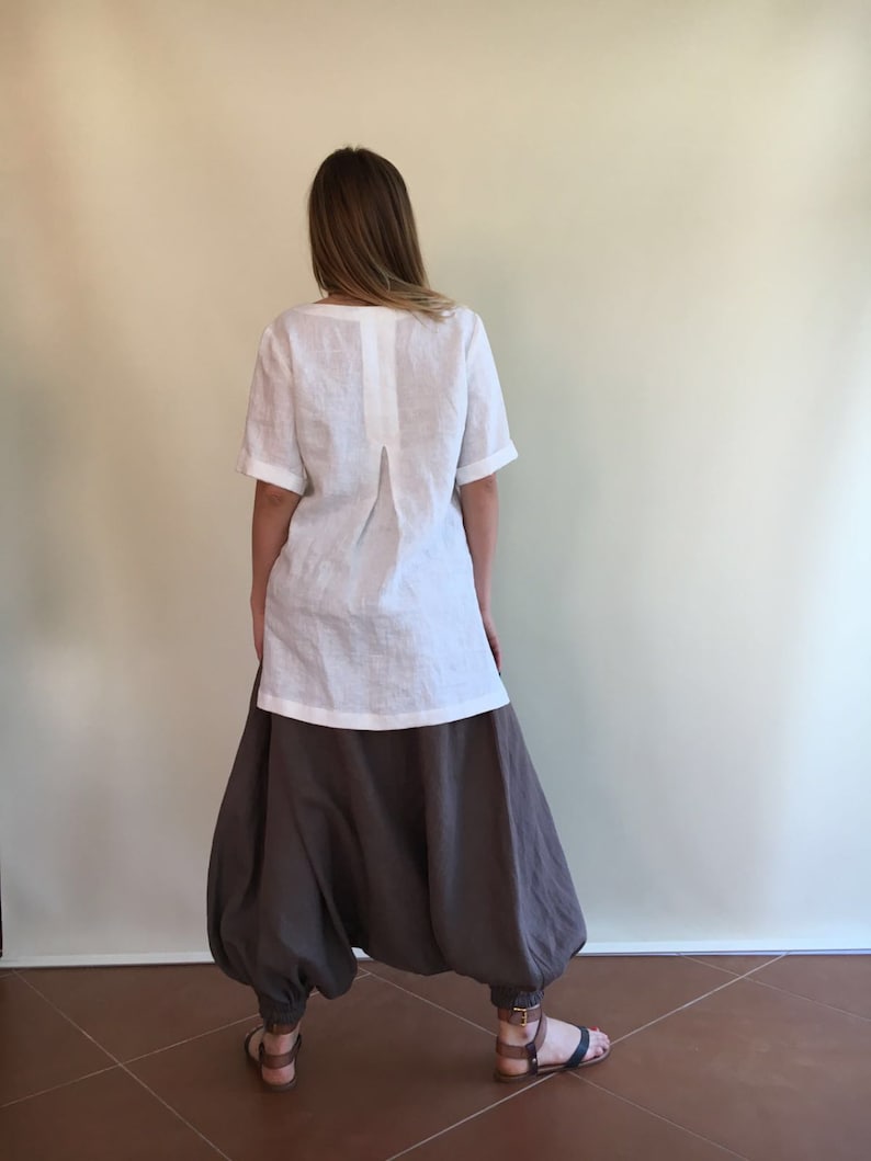 May include: A white linen top with a back pleat and short sleeves paired with brown linen pants. The pants have a wide leg and a gathered design.