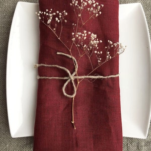 May include: A burgundy linen napkin folded and tied with twine, decorated with a sprig of dried white flowers.