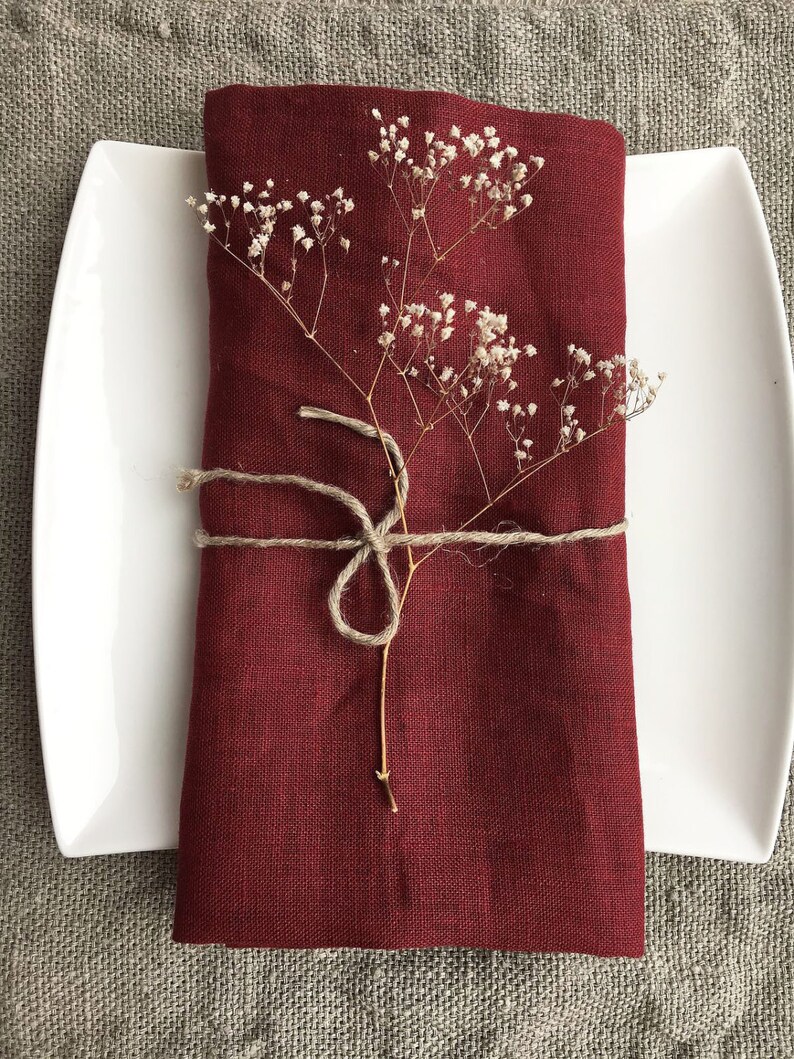 May include: A burgundy linen napkin folded and tied with twine, decorated with a sprig of dried white flowers.