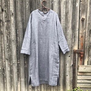 Op de afbeelding: Een grijs linnen shirt met witte strepen en een knoopsluiting aan de voorkant. Het shirt heeft lange mouwen en zijsplitten.