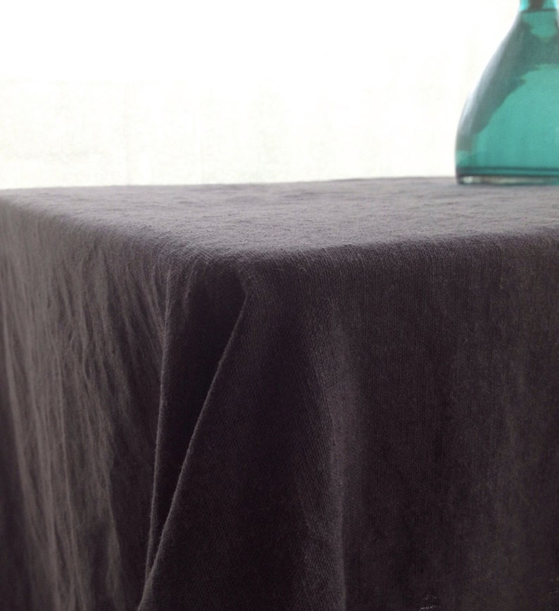 May include: A black linen tablecloth with a smooth, textured surface. The tablecloth is draped over a table and has a slight fold in the center.