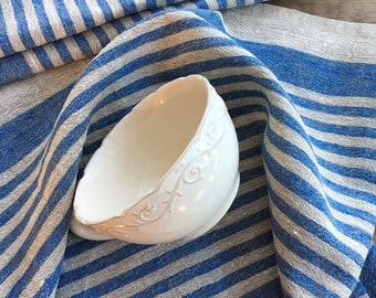 May include: A white ceramic bowl with a decorative design sits on top of a blue and white striped linen kitchen towel.