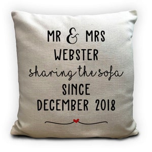 May include: A square, cream-coloured cushion with black text that reads "MR & MRS WEBSTER sharing the sofa SINCE DECEMBER 2018". A red heart is below the text. The cushion is a home decor item.
