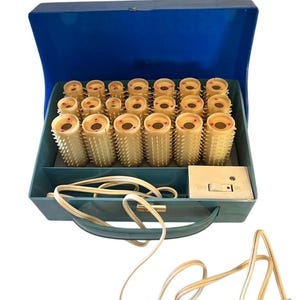 May include: A blue electric hair setter case containing twenty beige plastic hair rollers with textured spikes. The case features a white power switch with a small indicator light and a white electrical cord extending from the front.