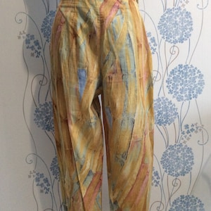 May include: A pair of wide-leg pants with a colorful abstract print in shades of yellow, blue, pink, and brown. The pants have a high waist and a relaxed fit.