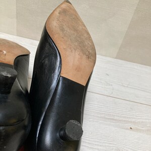 May include: A pair of black leather heeled shoes with pointed toes. The shoes have a small heel and a rubber sole.