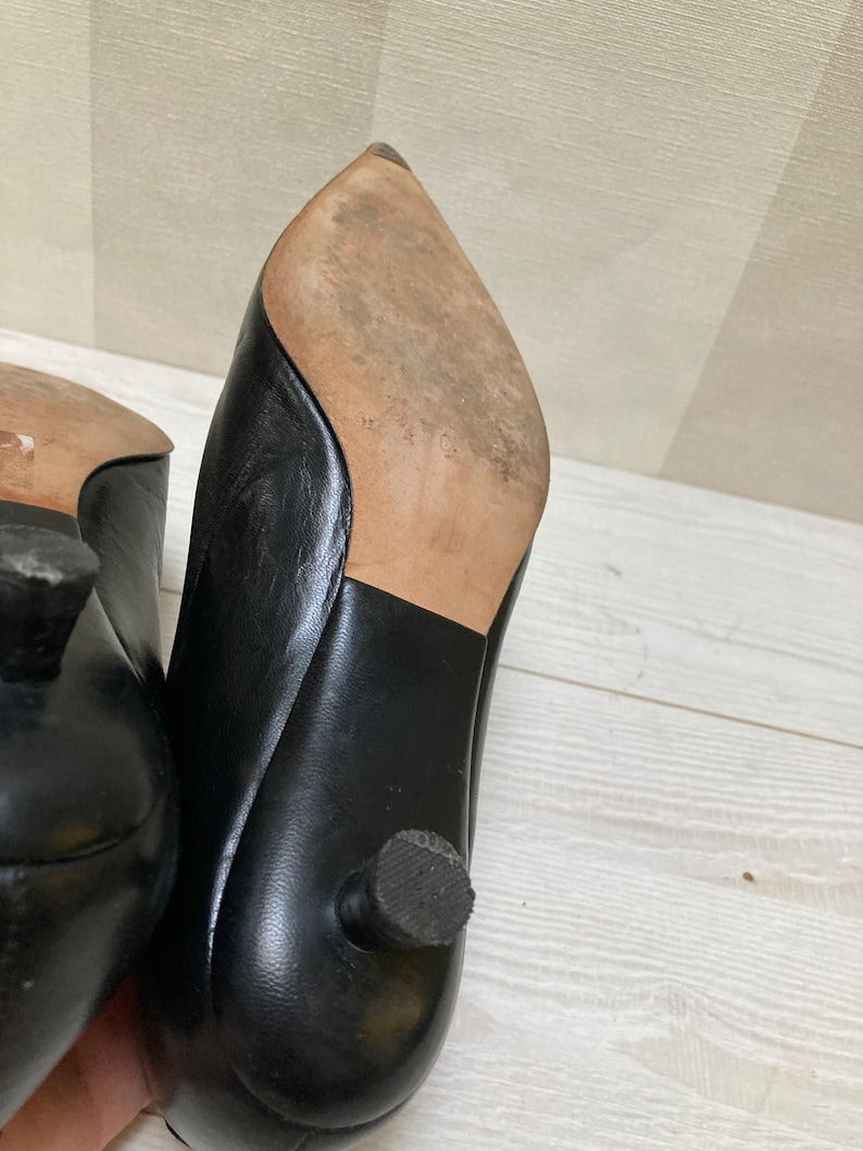 May include: A pair of black leather heeled shoes with pointed toes. The shoes have a small heel and a rubber sole.