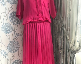 May include: A pink satin dress with a button-up top and a pleated skirt.