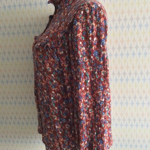 Pu&ograve; includere: Una blusa a maniche lunghe color ruggine con colletto a volant e stampa floreale in tonalit&agrave; blu, rosa e verde.