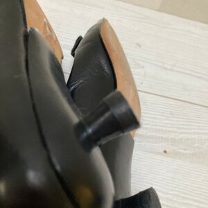 May include: Close-up of the black leather heels of a pair of shoes. The heels are a simple, block style with a rounded top.