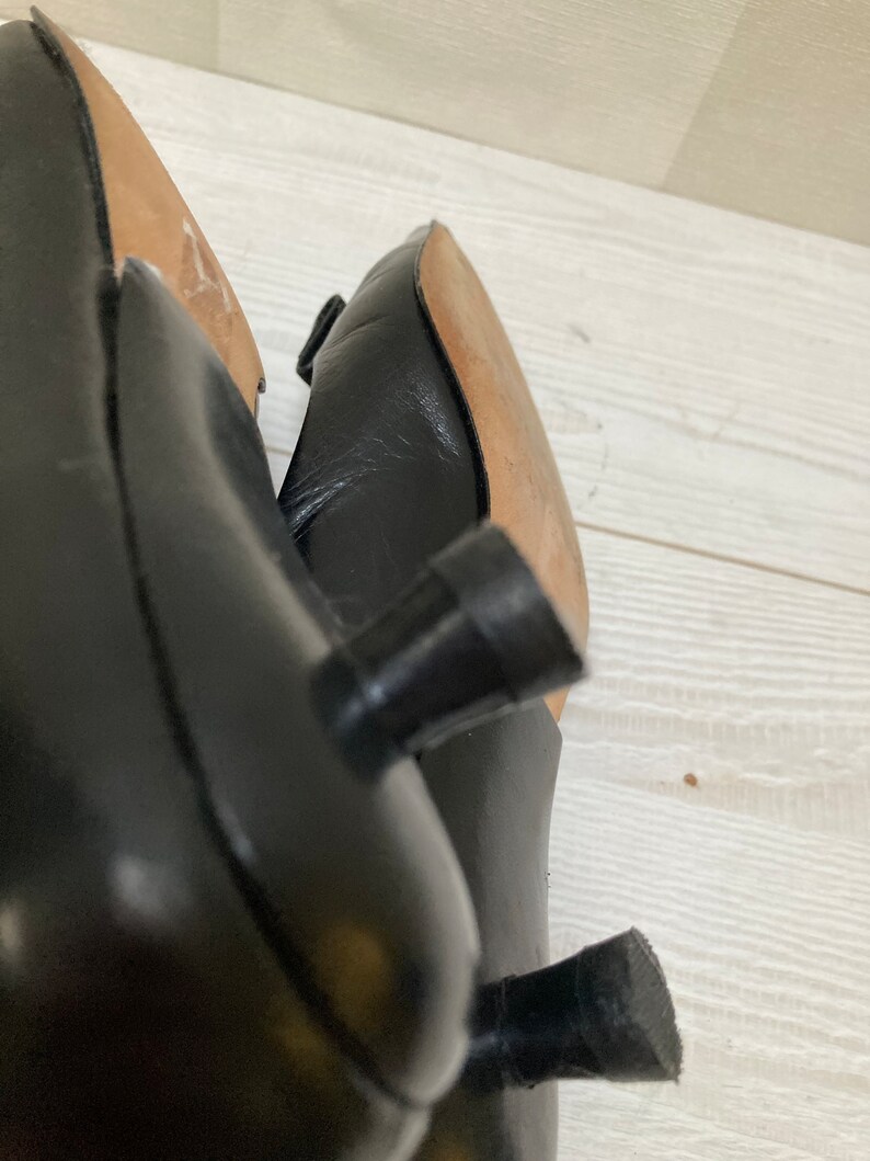 May include: Close-up of the black leather heels of a pair of shoes. The heels are a simple, block style with a rounded top.