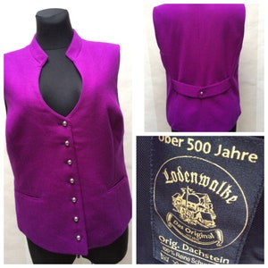 May include: A purple sleeveless waistcoat with a mandarin collar and silver buttons. The waistcoat has a label that reads "Uber 500 Jahre Lodenwolke Das Original Orig. Dachstein 100% Reine Schur"