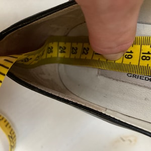 May include: Close-up of the inside of a black leather shoe with a yellow measuring tape showing a size of 23. The shoe is labeled "Grieder".