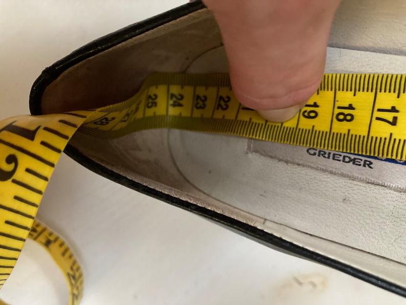 May include: Close-up of the inside of a black leather shoe with a yellow measuring tape showing a size of 23. The shoe is labeled "Grieder".