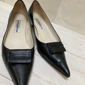 May include: A pair of black leather pointed-toe shoes with a small heel and a decorative buckle on the vamp. The shoes are labeled "Don Genie Boutique" and "2253 36".