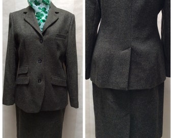 May include: A dark gray tweed skirt suit with a blazer and a skirt. The blazer has a notched collar, three buttons, and two flap pockets. The skirt is knee-length and has a straight silhouette.